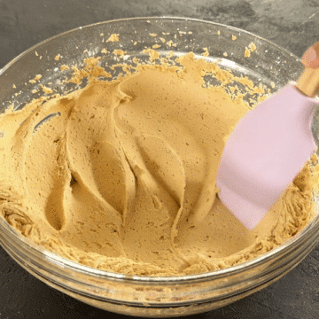 Spatula being used to smooth out icing in glass bowl. 